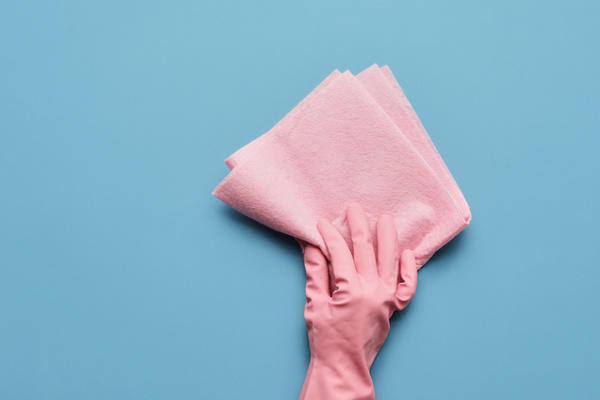 A pink viscose cleaning cloth is held in the hand in a pink rubber glove on a blue surface